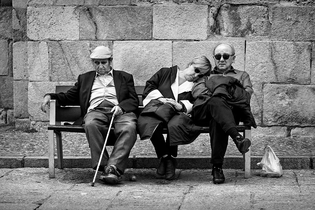 Three older people sitting together on a bench.